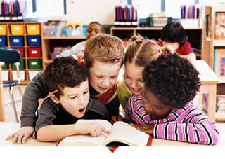 Four kids reading a book together in classroom